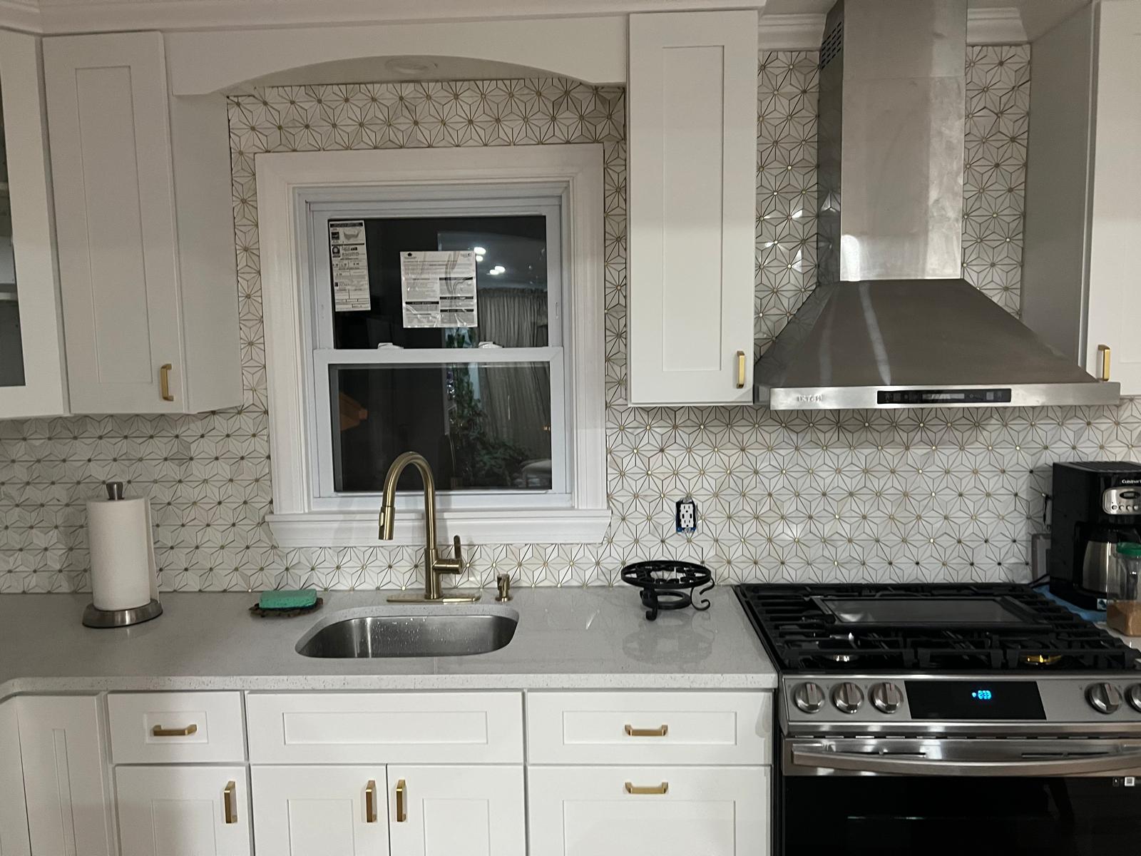 White kitchen with geometric backsplash, sink and stainless steel range hood